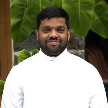 Man in white shirt standing in front of large green leaves.