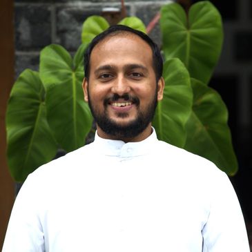 Smiling man in white shirt standing in front of large green leaves.