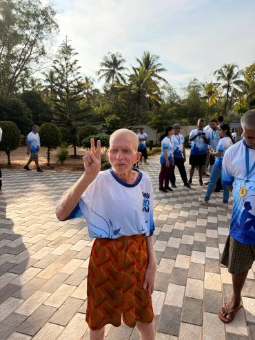 Elderly man flashing a peace sign at outdoor event.