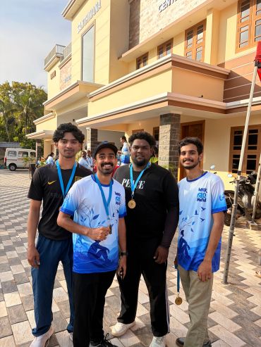 Four young men with medals posing outside a building.