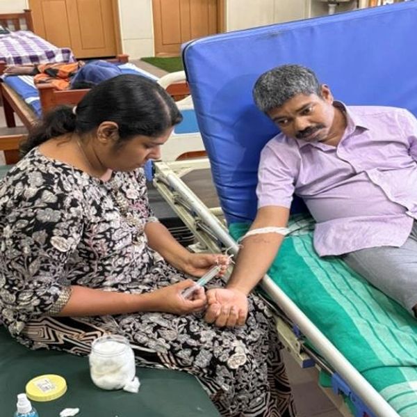 A woman is administering an injection to a man lying on a hospital bed.