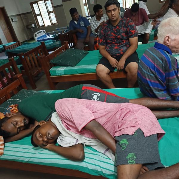 Several men resting and sitting on beds in a dormitory-like room.