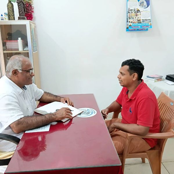 Two men engaged in a conversation across a desk in an office setting.