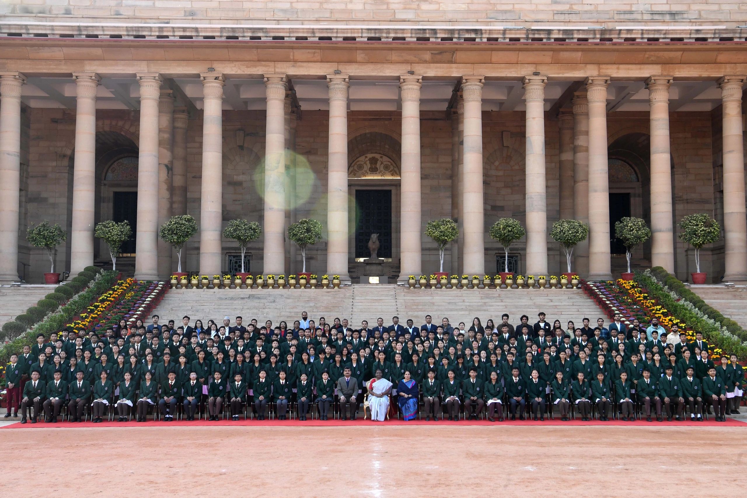 Large group photo of students in green blazers in front of a grand building.