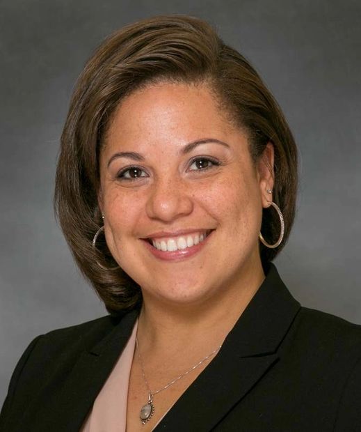 Headshot of light brown-skinned woman smiling and wearing a black blazer and pale pink blouse.