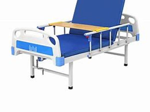 A blue adjustable hospital bed with a wooden overbed table.