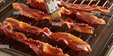 Strips of bacon being brushed with sauce on a grill rack.