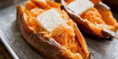 Baked sweet potatoes topped with melting butter on a tray.