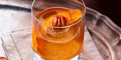 A glass of amber cocktail with a pecan garnish on a tray.