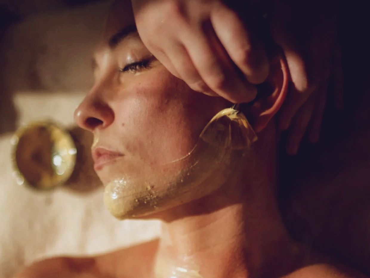 A woman having a golden facial mask applied near her chin and jawline.