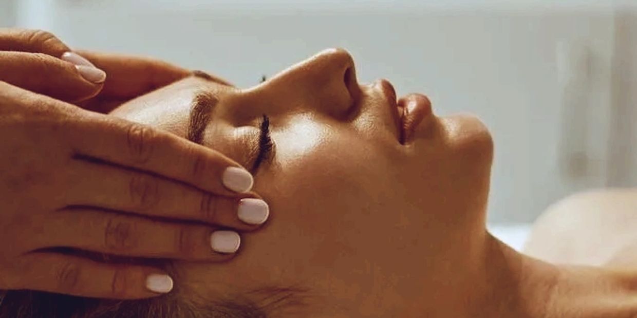 A person receiving a gentle forehead massage with closed eyes.