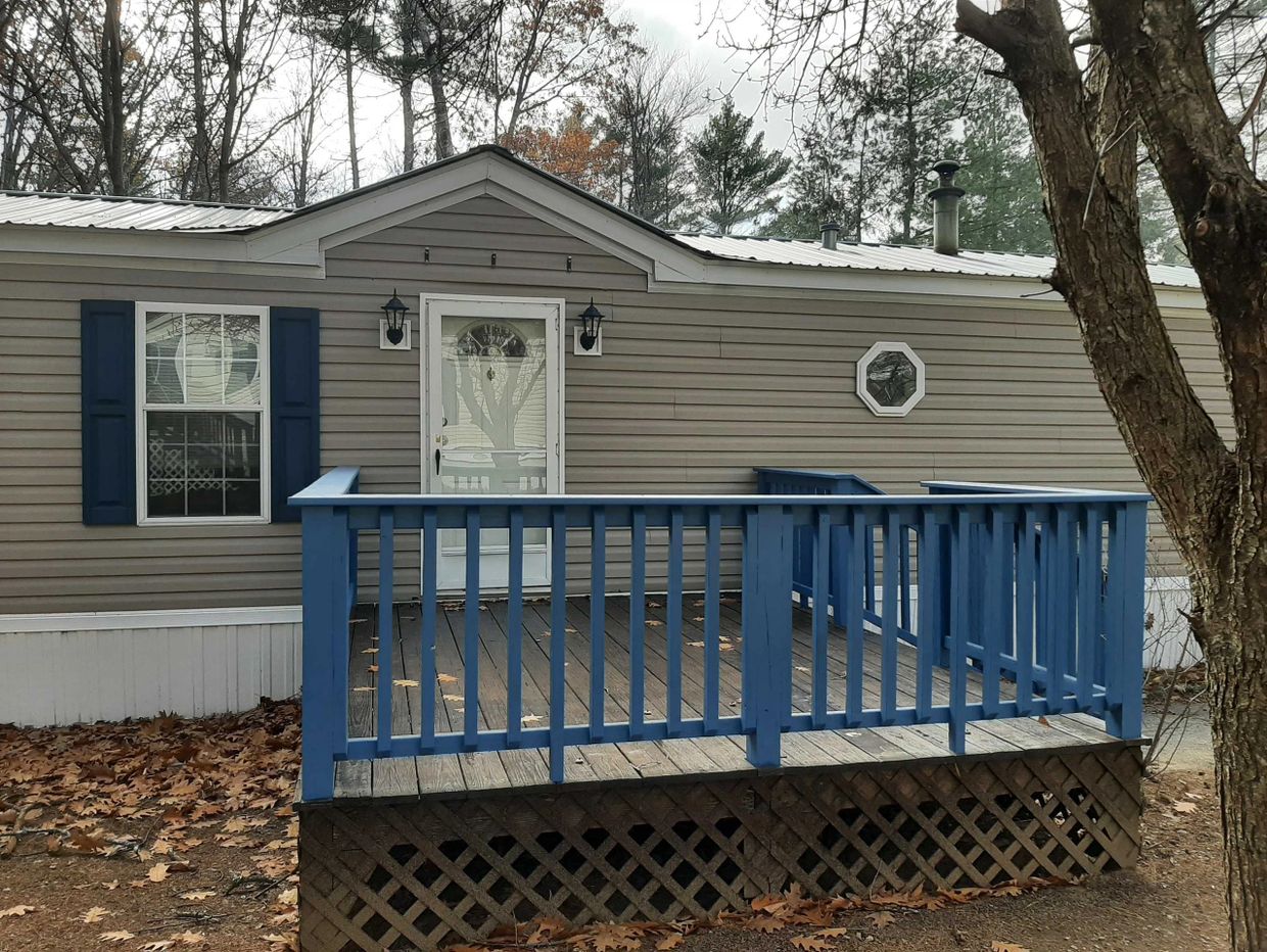 Small house with blue porch railing in a wooded area.