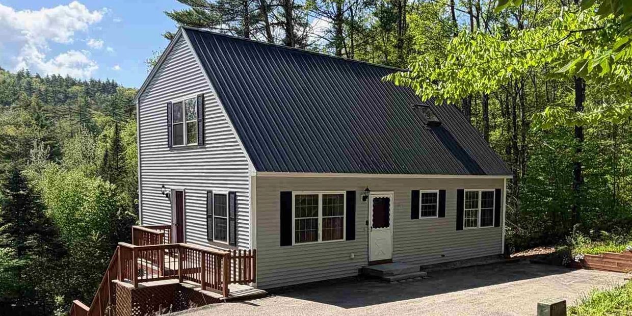 A charming house with black roof and white siding surrounded by green trees.