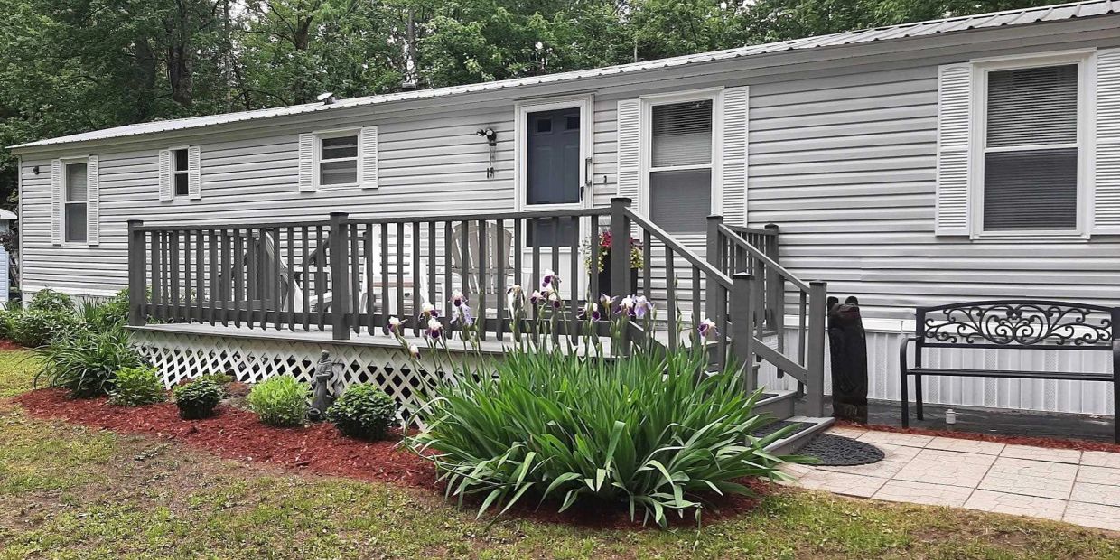 White mobile home with a wooden deck and flower garden in front.