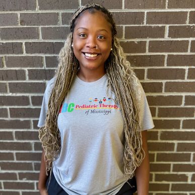 Smiling woman with long braided hair in front of a brick wall.