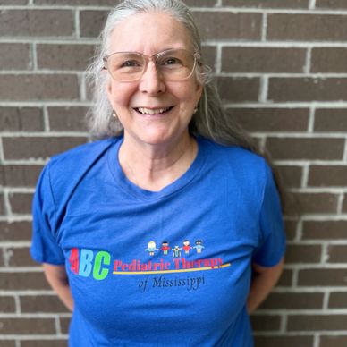 Smiling woman in a blue pediatric therapy T-shirt.