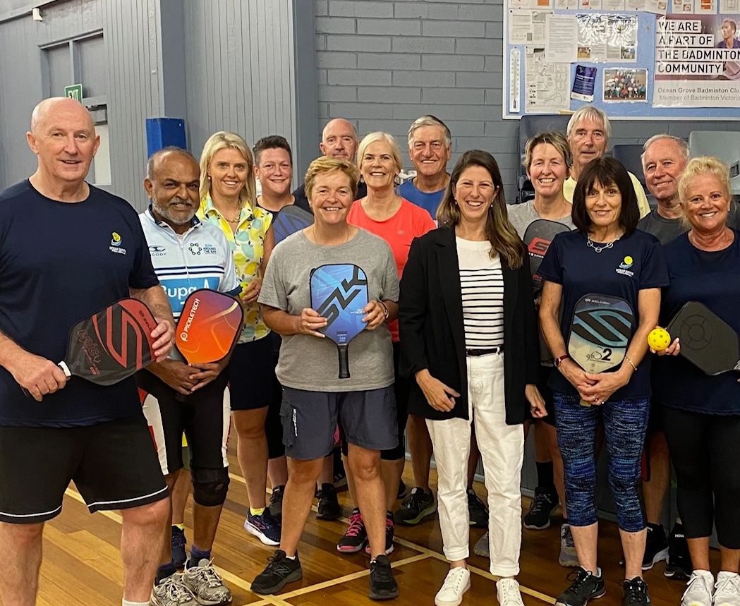 Group of adults posing with pickleball paddles in an indoor gym.