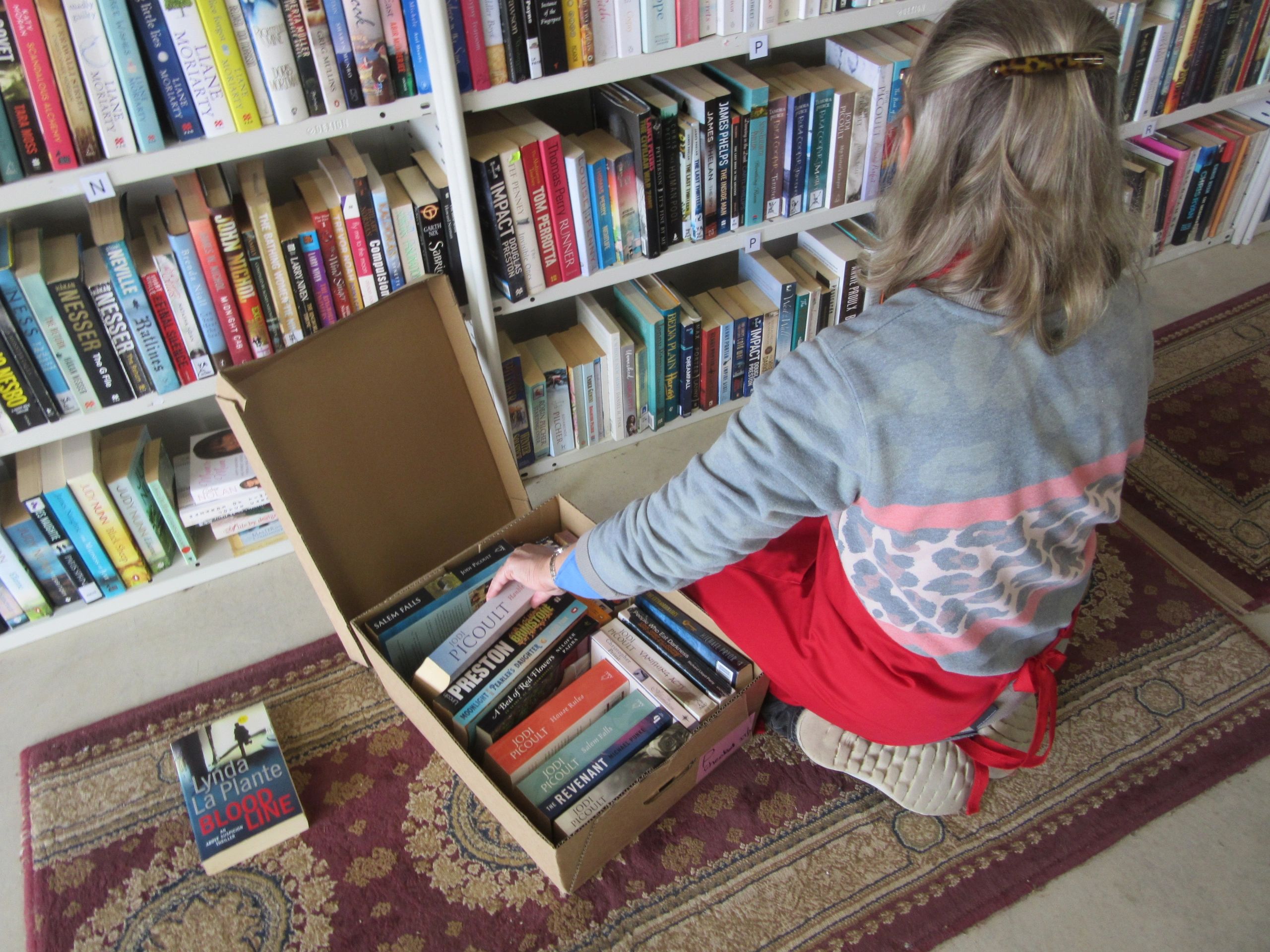 Person packing books into a box in a bookstore or library.