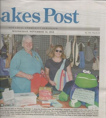 Two women at a local market booth with bags and a frog plush toy.