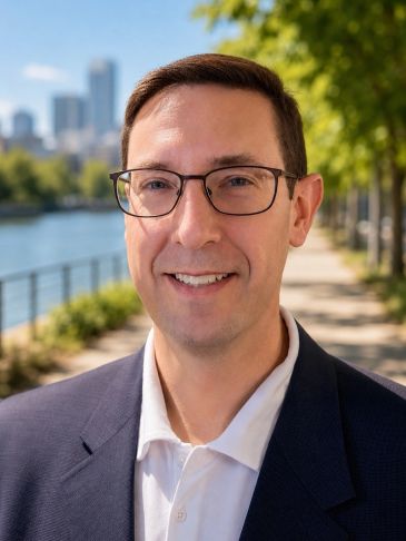 Smiling man outdoors near water with cityscape background.