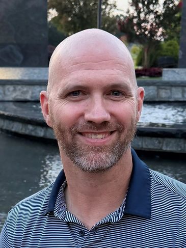 Smiling bald man with a beard outdoors.
