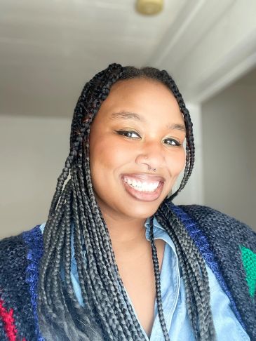 Smiling woman with braided hair and septum piercing.