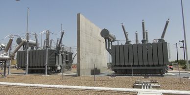 High-voltage electrical transformers separated by a concrete barrier in an outdoor substation.