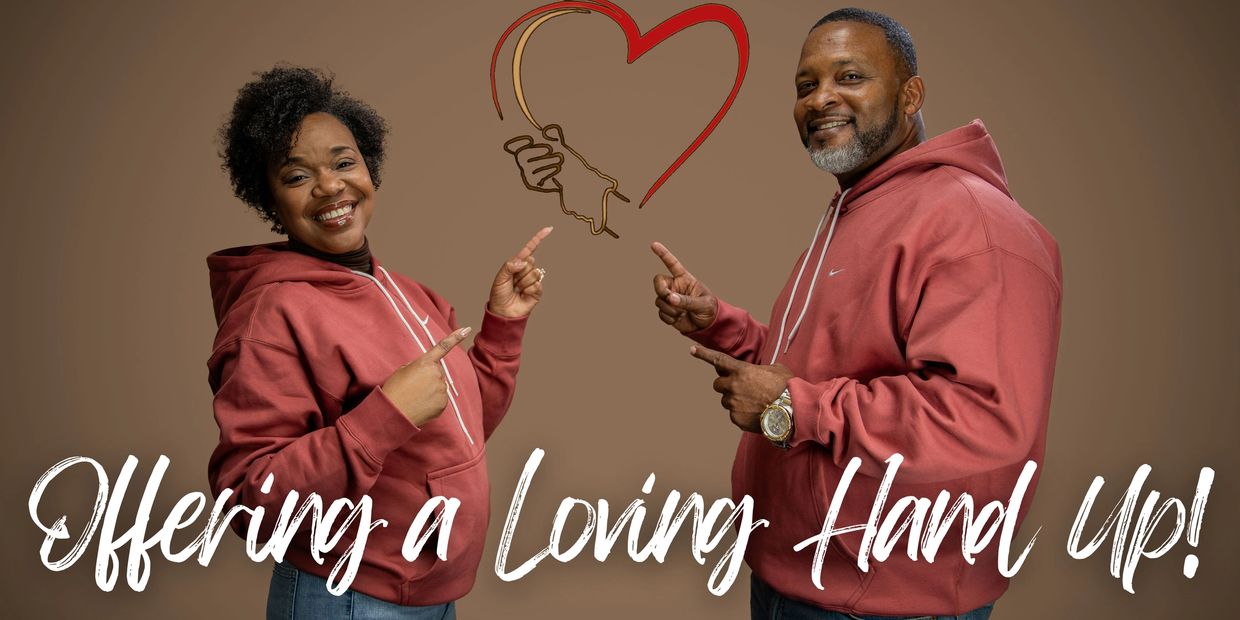 Couple smiling and pointing at a heart with linked hands, wearing matching hoodies.