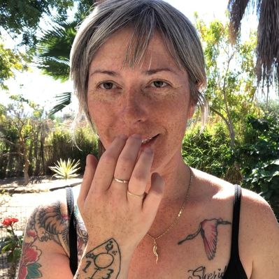 Woman with tattoos smiling outdoors in sunlight.