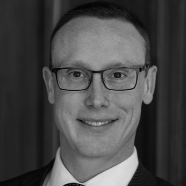 Black and white headshot of a smiling man wearing glasses and a suit.