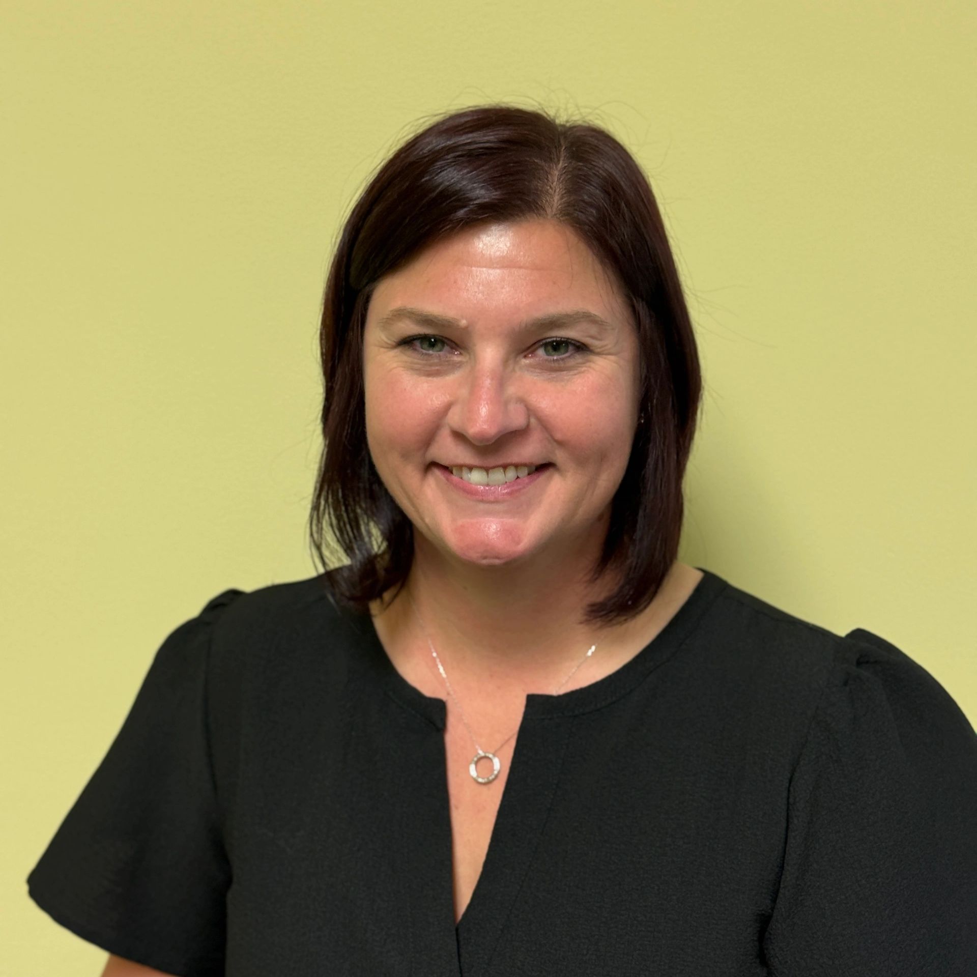 Smiling woman with dark hair against a plain yellow background.