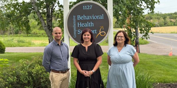Three people stand in front of a Behavioral Health Support sign outdoors.