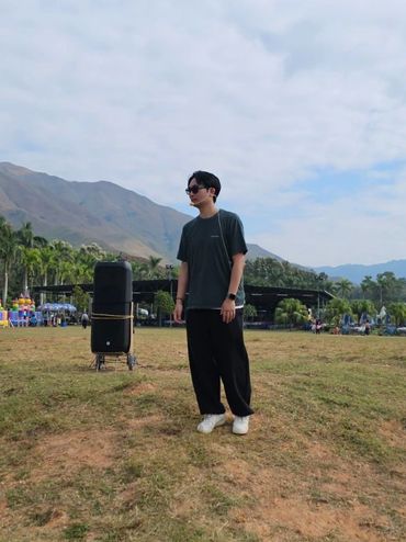 Two people standing on a grassy hill with mountains and sky in the background.