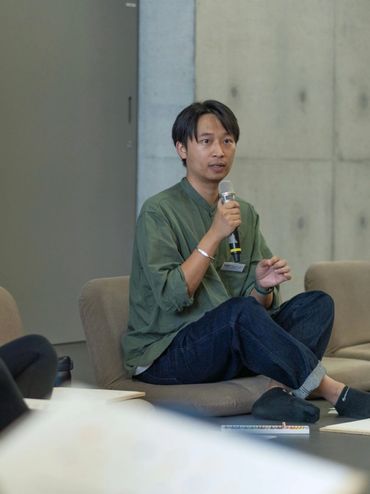 A man speaks into a microphone while seated during a discussion session.