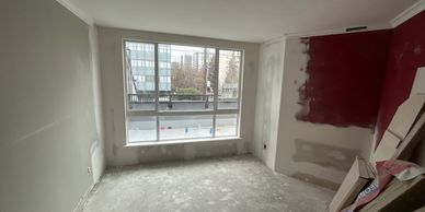An unfinished room with a large window and red paint on one wall.