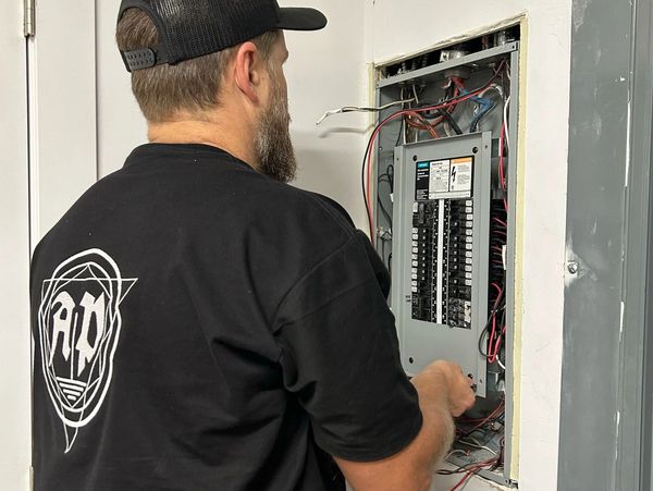 Man working on an electrical panel with wires exposed.