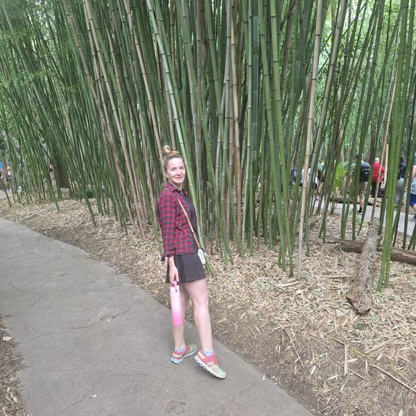 Woman in a red plaid shirt standing near a bamboo forest.
