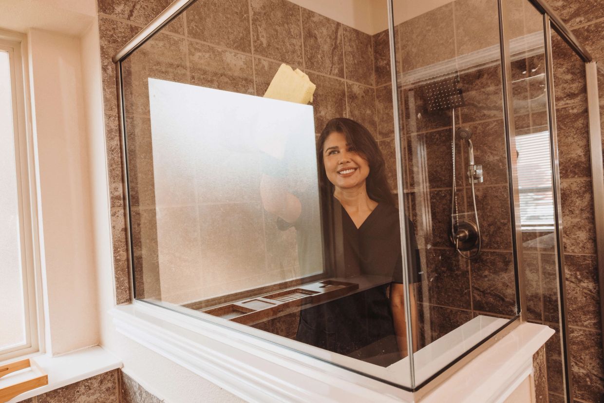 Aline at Grace Home Cleaning cleaning glass shower during bathroom cleaning service in Rockwall, TX