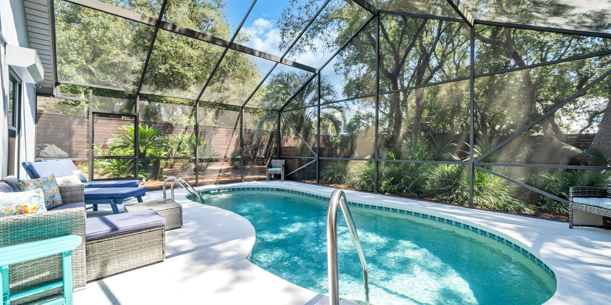 Bright screened-in pool area with lounge chairs and lush greenery.