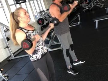 A couple performing bicep curls with barbells in the gym