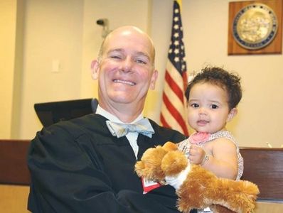 Judge holding a baby with a stuffed animal in a courtroom.