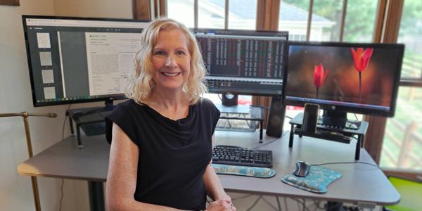 Woman smiling at her home office with three computer monitors.