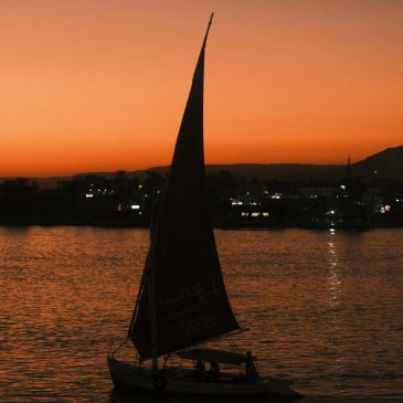 Sailboat silhouetted against an orange sunset over calm waters.