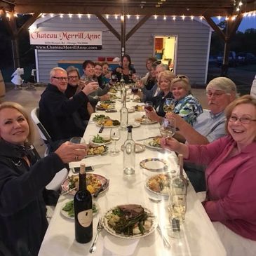 Picture of a long table with 14 smiling people sitting. They have raised glasses and are toasting.