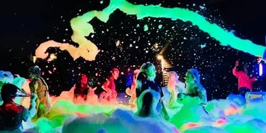 People enjoying a vibrant foam party with colorful lights at night.