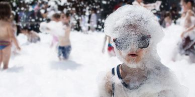 Child covered in foam wearing sunglasses at a foam party.