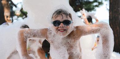 Child covered in foam wearing sunglasses and smiling.