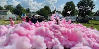 Children playing in a large foam pit filled with pink foam outdoors.
