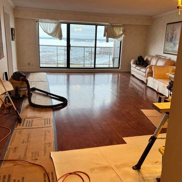 Living room with polished wooden floor and ocean view through large windows.