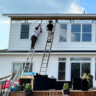 Two workers on ladders installing siding on a house exterior.